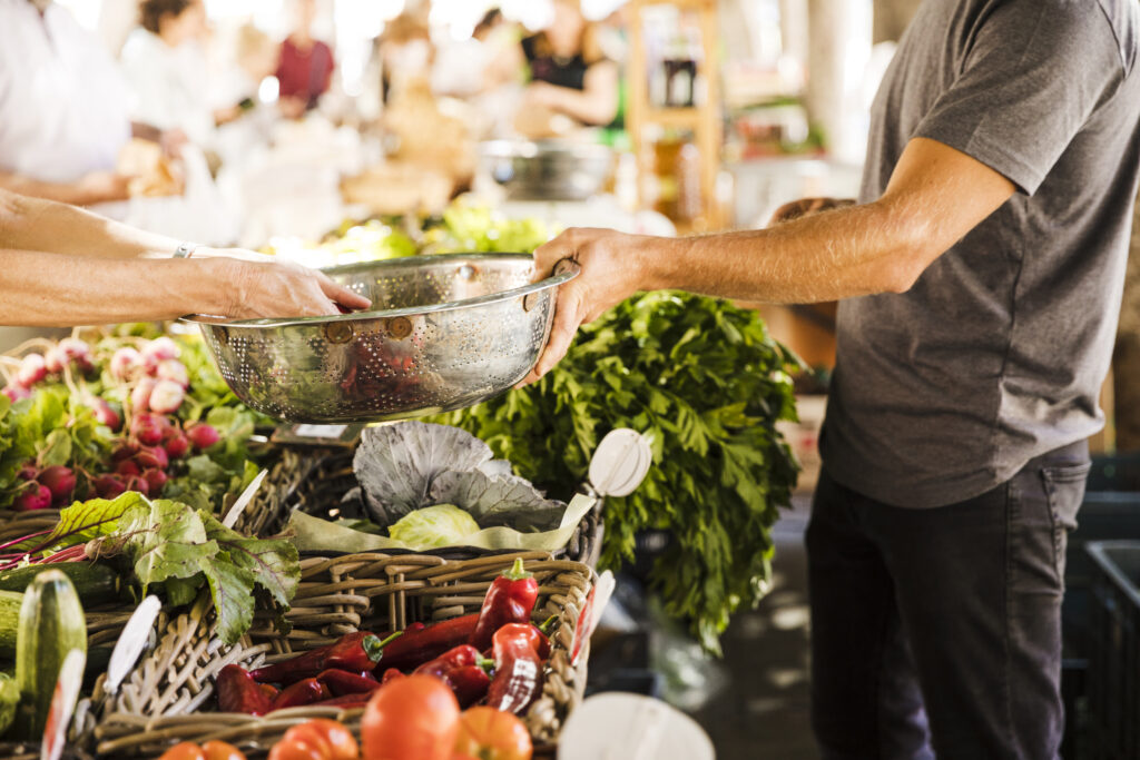 seller-hand-holding-stainless-steel-container-while-customer-buying-vegetable-market
